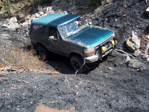 1996 Ford Bronco - A green 1995 Ford Bronco is shown off-roading on a steep, rocky, and coal-covered hill.