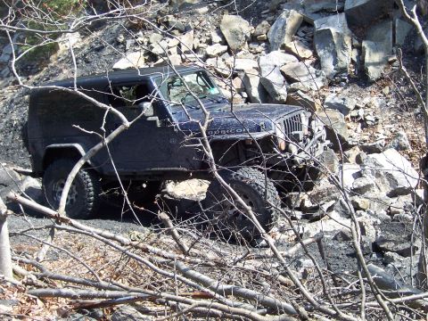 1996 Ford Bronco - A dark blue Jeep Wrangler Rubicon navigates a rocky, off-road trail.