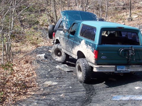 1996 Ford Bronco - Two muddy Broncos on a rocky trail, one with its hood up.
