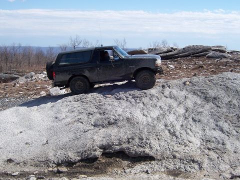 1996 Ford Bronco - A black Ford Bronco is parked on a rocky incline with a scenic view of hills and sky in the background.