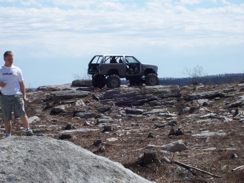1996 Ford Bronco - A heavily modified 1990s Ford Bronco sits atop a rocky hill, its roll cage and lifted suspension evident.