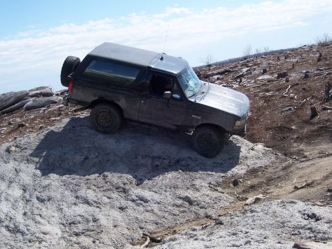 1996 Ford Bronco - A dark 1996 Ford Bronco navigates a rocky terrain on a sunny day.