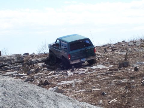 1996 Ford Bronco - A green Ford Bronco navigates a challenging rocky trail under a bright sky.