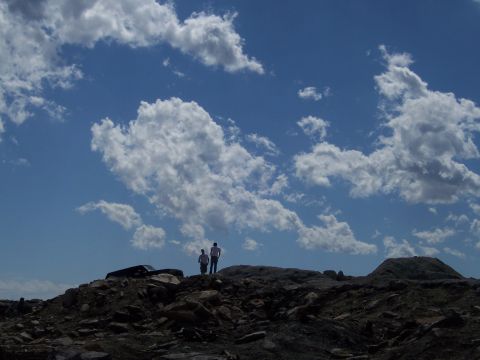 1996 Ford Bronco - Two figures stand atop a desolate, rocky landscape beneath a vast, cloud-filled sky.