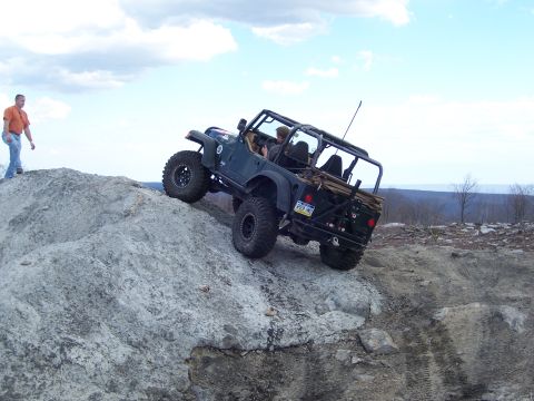 1996 Ford Bronco - A dark green Jeep Wrangler navigates a steep, rocky incline on an off-road trail.