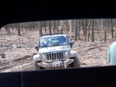 1996 Ford Bronco - Jeep Wrangler navigating muddy terrain in a dense forest with bare trees.