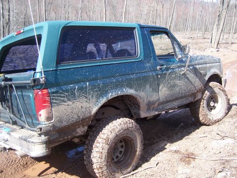 1996 Ford Bronco - This heavily soiled teal Ford Bronco navigates a muddy, wooded terrain.