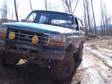 1996 Ford Bronco - Muddy 1996 Ford Bronco navigates a rough, wooded off-road path.