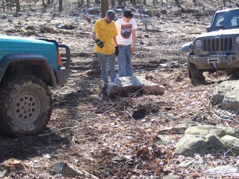 1996 Ford Bronco - Two people assess the terrain next to two off-road vehicles in a wooded, muddy area.