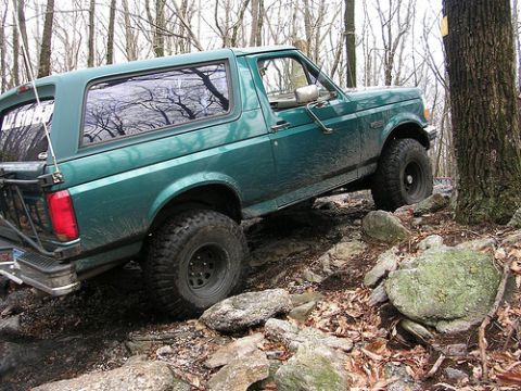1996 Ford Bronco - A green 1996 Ford Bronco navigates a challenging rocky terrain on an off-road trail.