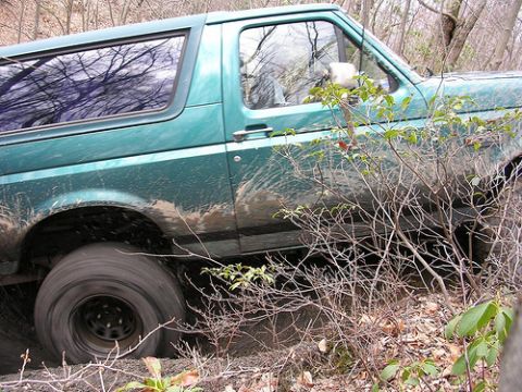 1996 Ford Bronco - Green SUV navigating rough terrain with mud splashing from the tires.