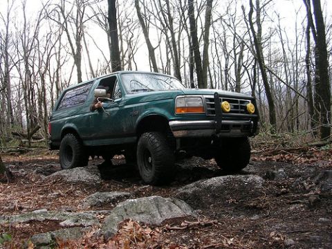 1996 Ford Bronco - A green 1996 Ford Bronco navigates a rocky path through a wooded area.