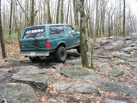 1996 Ford Bronco - Green 1996 Ford Bronco navigating a challenging rocky trail in a wooded area.