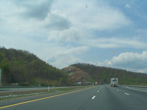 1998 Ford Taurus - A view from a vehicle driving on a highway with trucks in the distance and tree-covered hills.