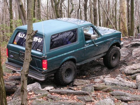 1996 Ford Bronco - A green 1996 Ford Bronco navigates a rocky, wooded trail.