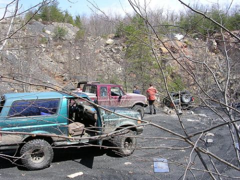 1996 Ford Bronco - Several off-road vehicles are parked on a dirt surface with rocky hills in the background.