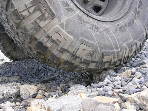 1996 Ford Bronco - A close-up, low-angle shot shows the tread of a large, off-road tire on a vehicle, resting on a pile of gravel and rocks. The tire has a ru…