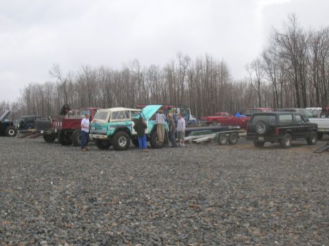 1996 Ford Bronco - A group of people stand around several off-road vehicles parked on a gravel lot. A turquoise and white SUV with large tires is the focus, w…