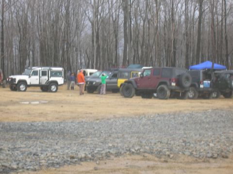 1996 Ford Bronco - A line of off-road vehicles are parked in a grassy area with a bare tree forest in the background. A white SUV is parked on the left, follo…