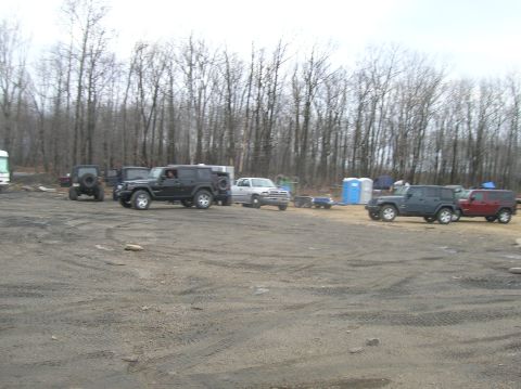 1996 Ford Bronco - Several off-road vehicles are parked in a dirt lot with a wooded area in the background. A black Jeep Wrangler is in the foreground, with a…