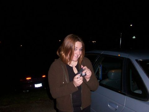 1998 Ford Taurus - A woman stands next to a car at night, holding a camera, with another vehicle visible in the dark background.
