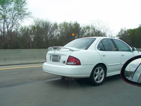 1998 Ford Taurus - A white sedan with a spoiler drives down the highway on a cloudy day.