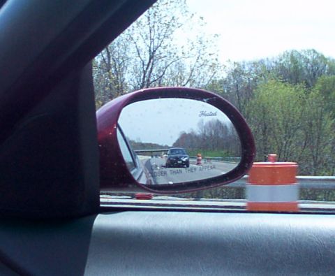 1998 Ford Taurus - Side mirror view of a car on the highway with a traffic barrel nearby.