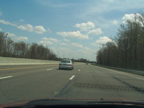 1998 Ford Taurus - A silver sedan travels down a highway under a partly cloudy sky.