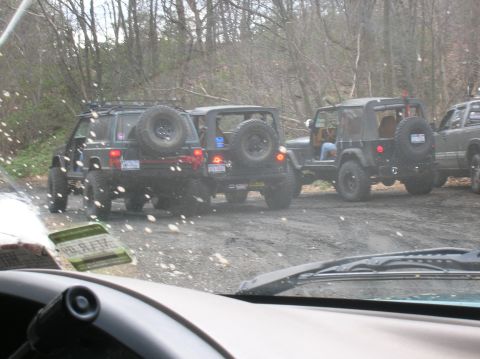 1996 Ford Bronco - Three Jeep SUVs are parked on a dirt road surrounded by trees. The front Jeep is dark green with a spare tire mounted on the rear. The midd…