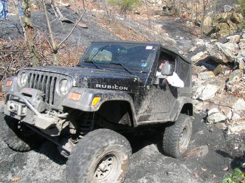 1996 Ford Bronco - A black Jeep Wrangler Rubicon is navigating a rocky, off-road trail. The vehicle is covered in mud, indicating it is actively being used fo…