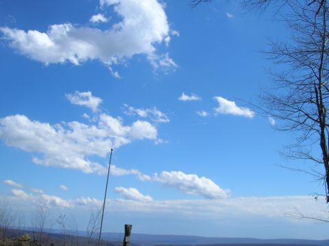 1996 Ford Bronco - A bright blue sky with scattered white clouds is visible above a distant landscape of rolling hills. A tall, thin antenna or pole stands ve…