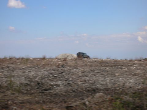 1996 Ford Bronco - A dark-colored SUV, possibly a Jeep, is parked on a barren, logged landscape under a blue sky with scattered clouds.