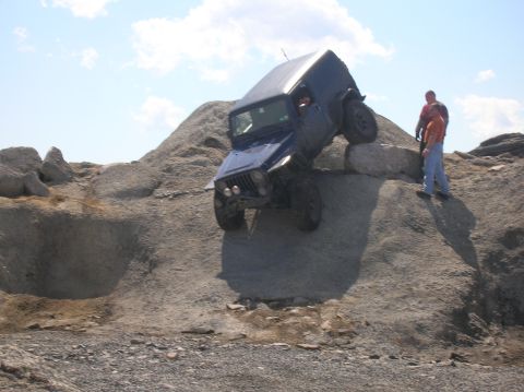 1996 Ford Bronco - A blue Jeep Wrangler is angled precariously on a large rock formation, with two people watching from the top of the formation.