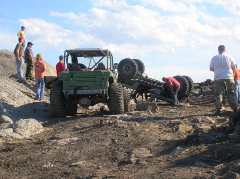 1996 Ford Bronco - A green off-road vehicle is parked on a rocky terrain with another off-road vehicle flipped on its side nearby. Several people are observin…