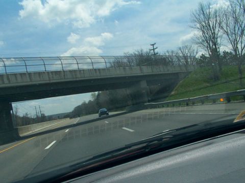 1998 Ford Taurus - A dark sedan travels on the highway beneath a concrete overpass on a cloudy day.