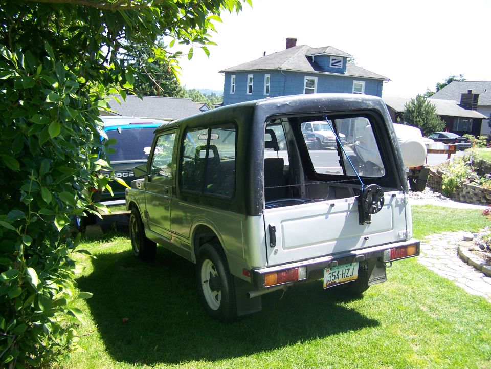 Rear view of silver Suzuki Samurai on lawn with houses and trees behind