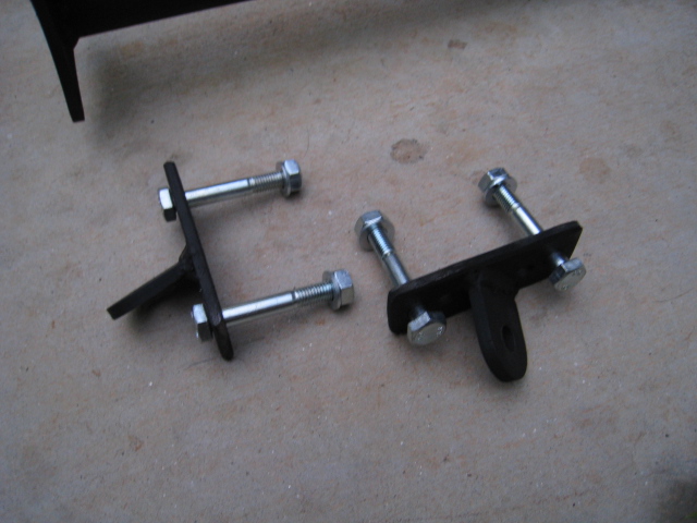 Pair of black steel suspension brackets with zinc bolts on a concrete floor