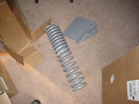 1995 Ford Bronco - A suspension coil and a metal bracket are shown on a carpeted floor, with cardboard boxes nearby.