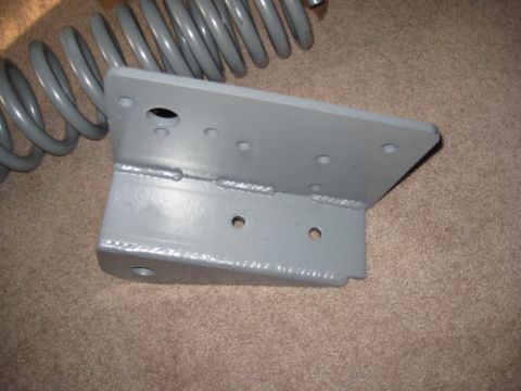 1995 Ford Bronco - A gray suspension coil and a metal bracket with multiple holes and welds are shown on a carpeted floor.