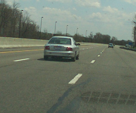 1998 Ford Taurus - A silver sedan is seen from behind on a multi-lane highway under a partly cloudy sky.