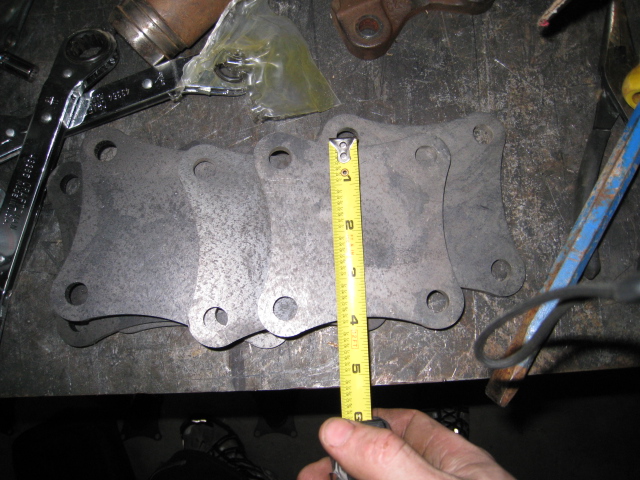 Hand measuring two multi-hole steel bracket plates with a tape measure on a bench