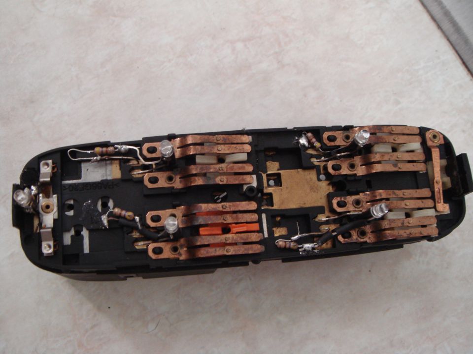 Opened black switch assembly showing copper contacts, resistors, bulbs and solder repairs on a tile floor