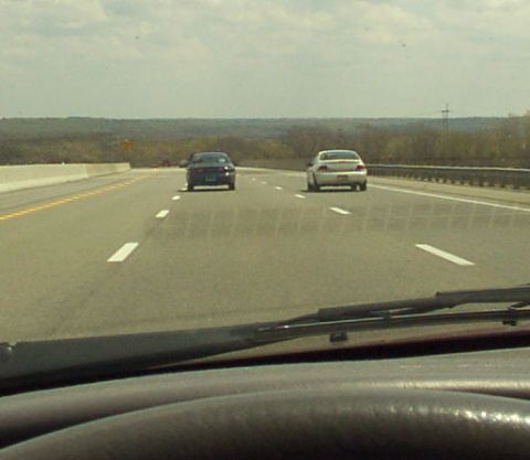 1998 Ford Taurus - Two cars drive down a highway under a cloudy sky.