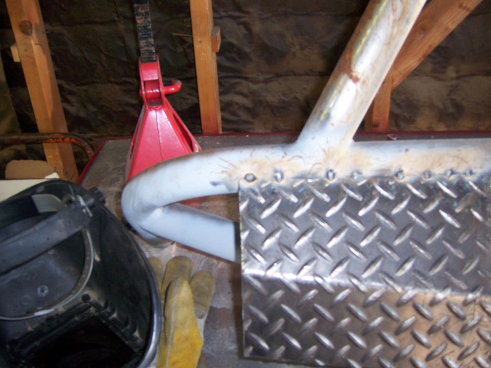 Welding mask, gloves, and a red jack near a custom metal bumper being fabricated