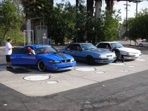 1990 Ford Mustang - A blue 2000 Ford Mustang is parked with its door open, alongside two other Mustangs.