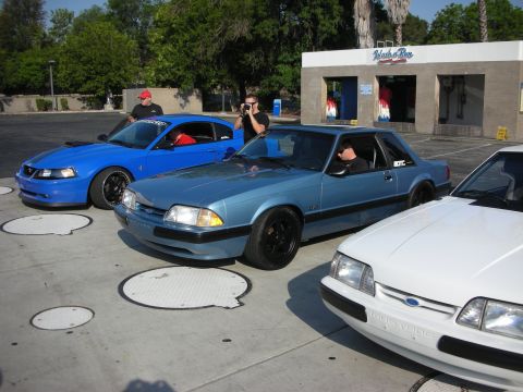 1990 Ford Mustang - Three Ford Mustangs are parked in front of a car wash. The middle car is a blue 1990 model.