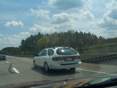 1998 Ford Taurus - A white station wagon is driving on the highway under a cloudy sky.