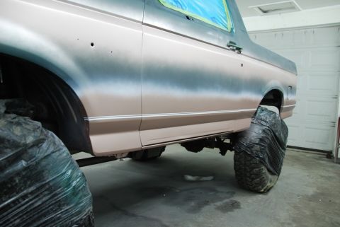 1996 Ford Bronco - A vehicle's side is shown, covered in primer and masking tape, with tires protected during the painting process.