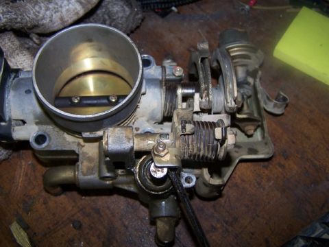 2000 Nissan Xterra - Close-up view of a dirty throttle body assembly, likely for a vehicle engine.