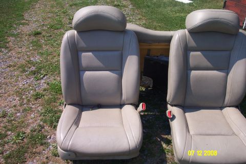 1992 Ford Bronco - Pair of tan leather car seats with headrests and seatbelt buckles, photographed outdoors.
